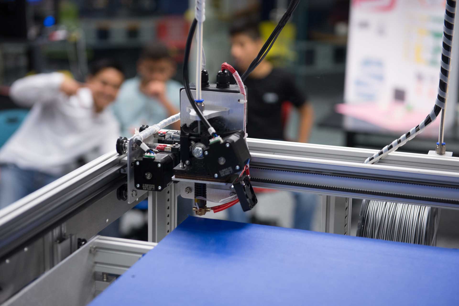 A 3d printer in the foreground, with students posing in the background