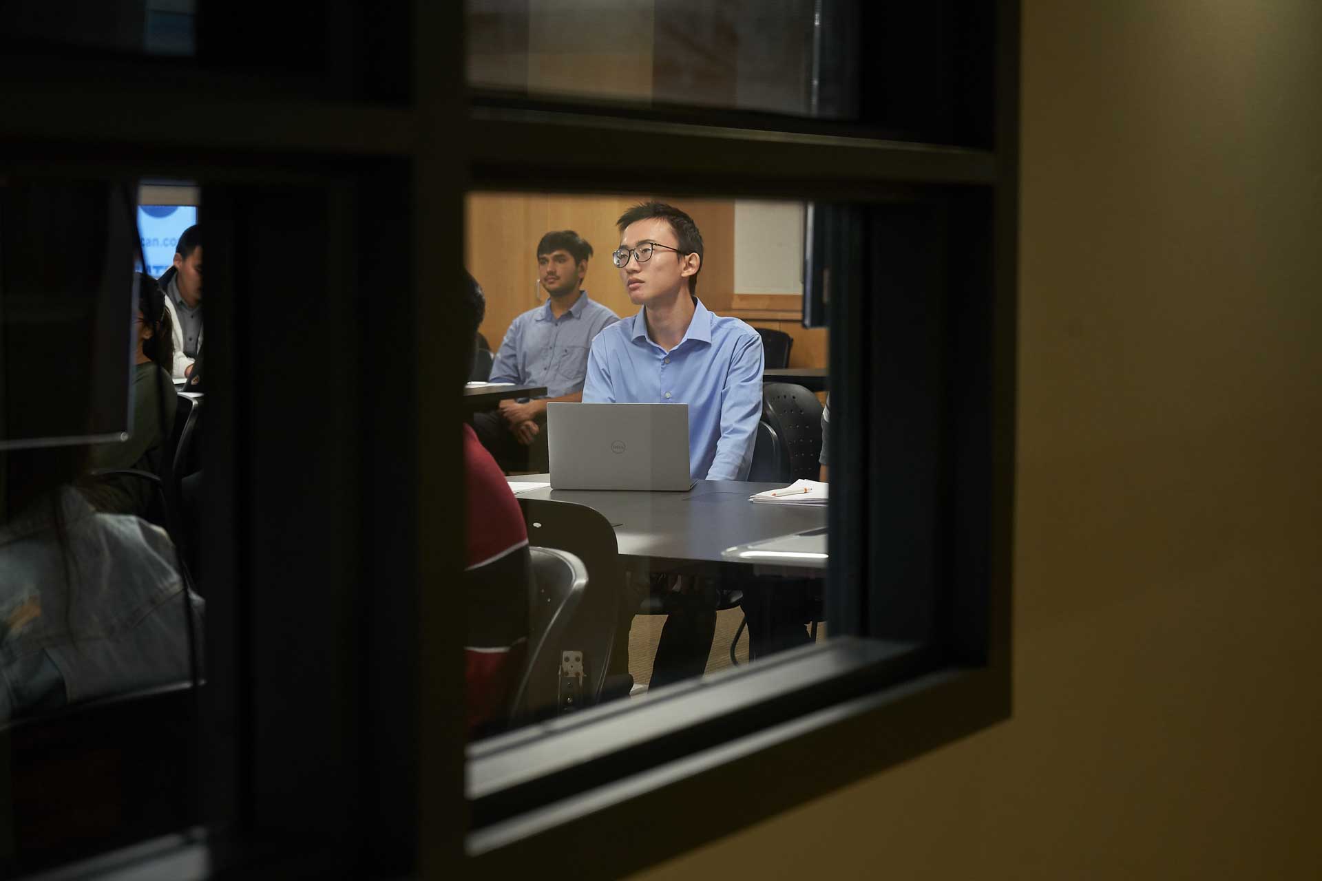 A student pays attention in class, seen through a window