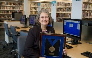 Jean Armour-Polly sits in library with her award